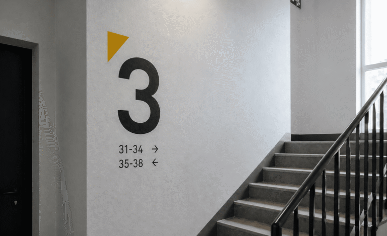 Oznakowanie klatki schodowej z dużą czarną cyfrą 3 i numerami lokali na jasnej ścianie.