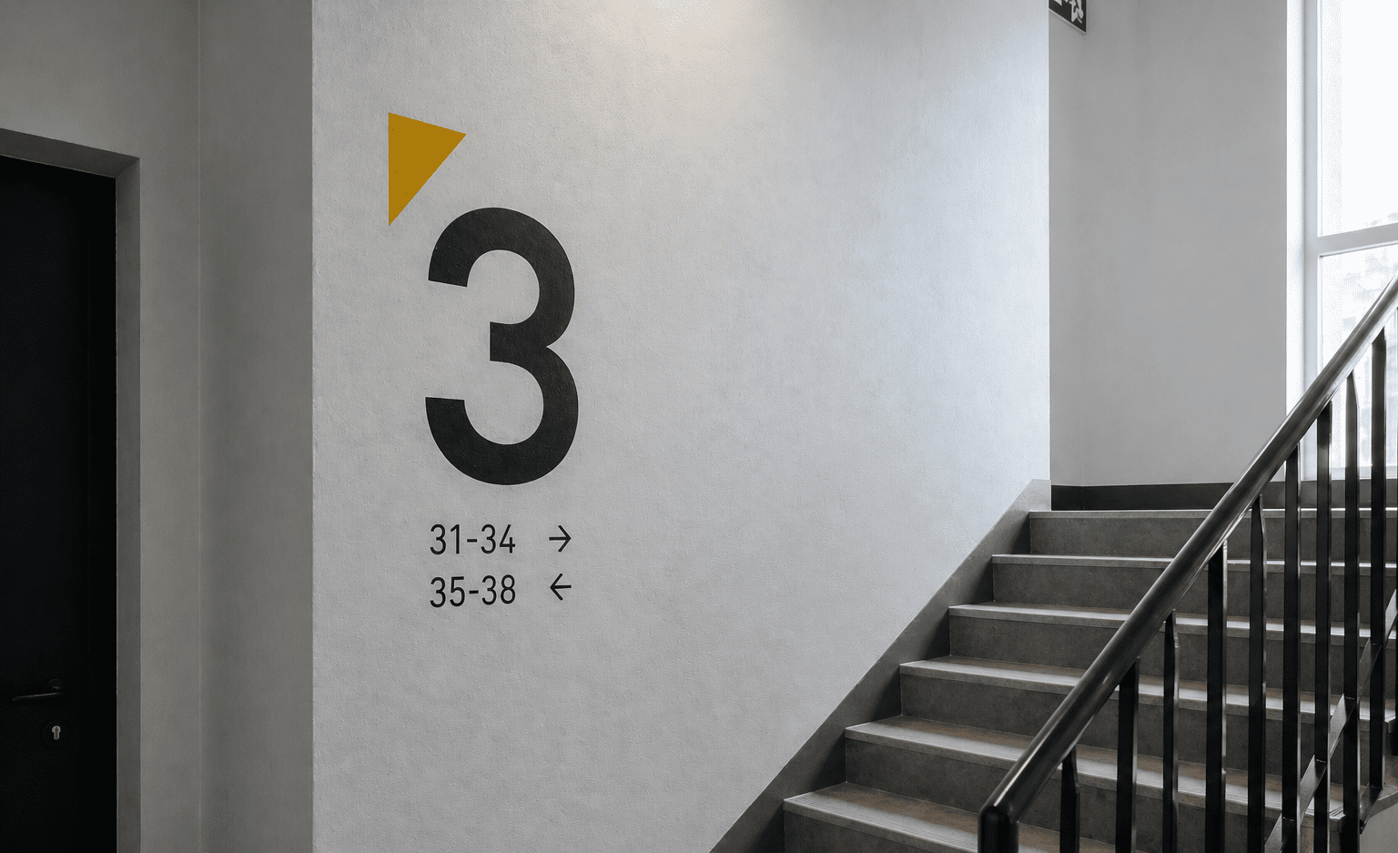 Minimalistyczne oznakowanie klatki schodowej z dużą czarną cyfrą 3 i numerami lokali na jasnej ścianie.